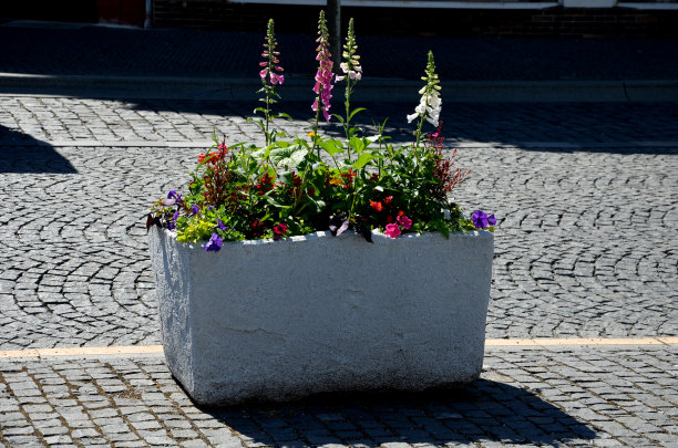 多年生花坛与一年生植物在花坛边缘铺上花岗岩鹅卵石镇广场，石柱靠入口和石槽和花盆植物图片下载