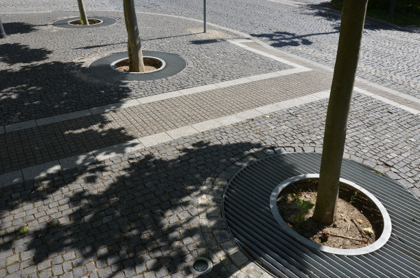 多年生花坛与一年生植物在花坛边缘铺上花岗岩鹅卵石镇广场，石柱靠入口和石槽和花盆植物图片下载