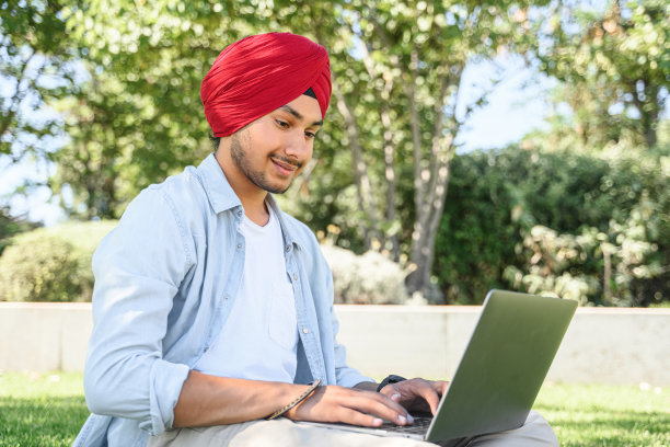戴着头巾的乐观民族男子坐在草坪上使用笔记本电脑图片下载
