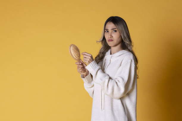 年轻的亚洲女子在卷发梳头发的黄色背景图片下载