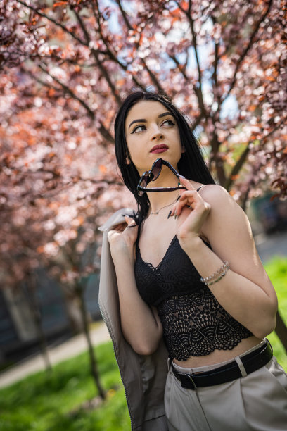 穿着白色皮夹克的时髦女人在春天花园的樱花附近摆姿势图片下载