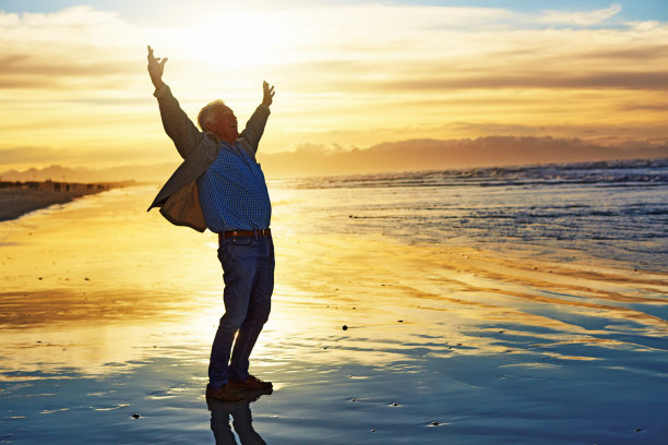 生活是伟大的!老人站在田园诗般的海边，举起双臂迎接黎明图片下载