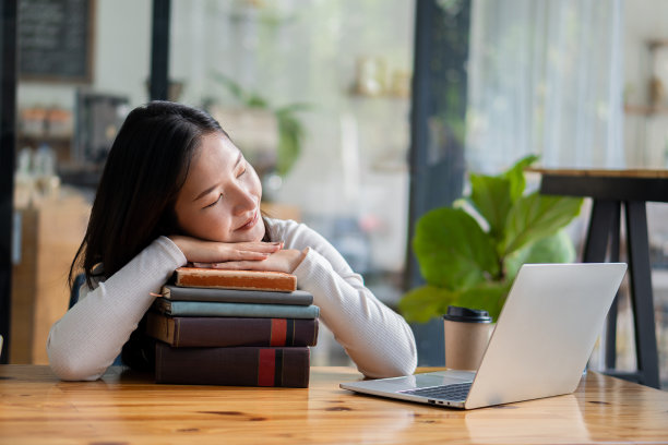 一名年轻的亚洲学生在笔记本电脑上在线上课时，把头靠在书桌前的虎皮上。图片下载