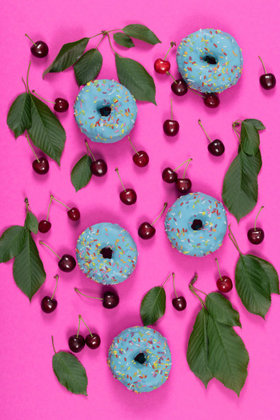 粉红色的背景和静物，脆的红色樱桃，樱桃叶和蓝色甜甜圈并排躺着图片下载