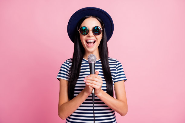 照片肖像唱歌的女孩手持麦克风在两个手中孤立的粉彩背景图片下载
