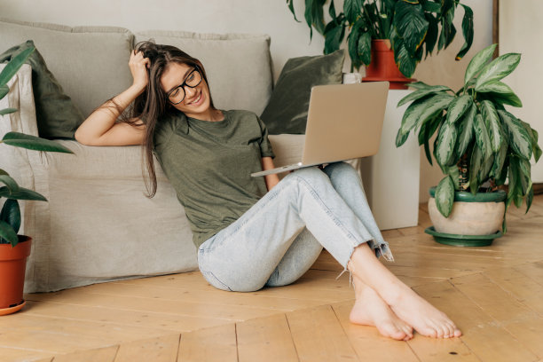 年轻迷人的无忧无虑的女人坐在地板上视频聊天在线笔记本电脑。图片下载
