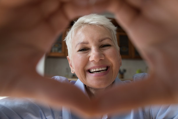 快乐微笑的老太太看着相机在手指心里图片下载