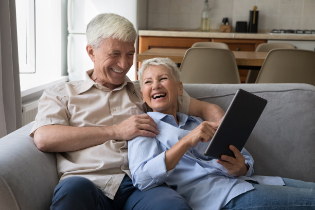 兴奋的老祖父母抱在沙发上用数字触控板大笑图片下载