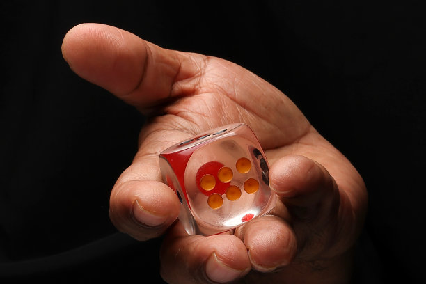 亚洲男性深色皮肤单手拳头手指在黑色背景上持有透明的丙烯酸塑料玩骰子图片下载