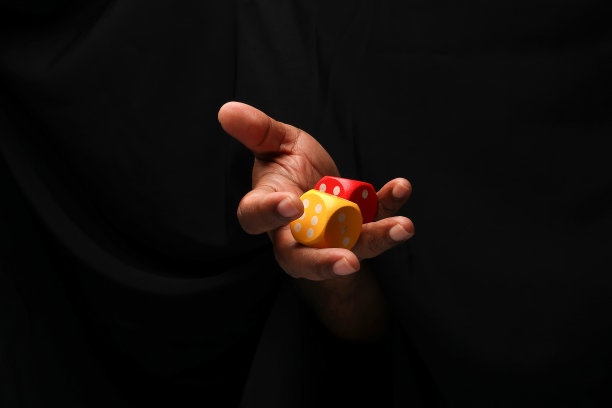 亚洲男性深色皮肤的单手拳头手指在黑色的背景上持有木制的红黄色玩骰子图片下载