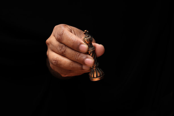 亚洲男性深色皮肤单手握拳手指在黑色背景上持有游戏金属棋王图片下载