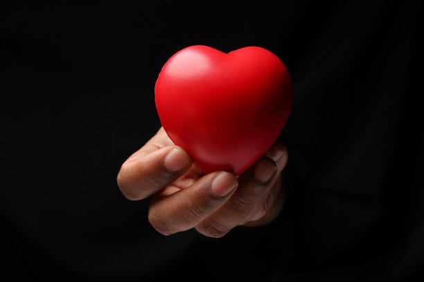 亚洲男性深色皮肤单手拳头手指在黑色背景上持有红色橡胶鹿爱形状图片下载