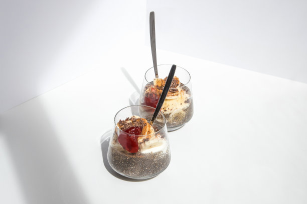 从鼠尾草植物中提取的奇亚籽，非常健康，可以用于许多食谱中。杯子里装着水合的种子和天然酸奶，香蕉，草莓酱，肉桂粉和巧克力屑。图片从上面看到的白色背景。复制的年代图片下载