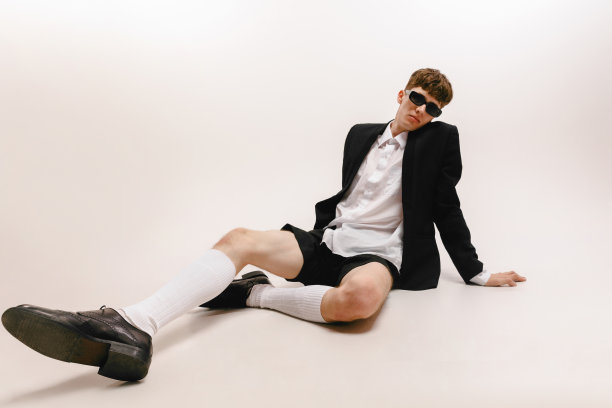 年轻时尚男子的广角视野，学生坐在地板上孤立在白色的工作室背景。时尚、青春、情感、艺术的概念图片下载