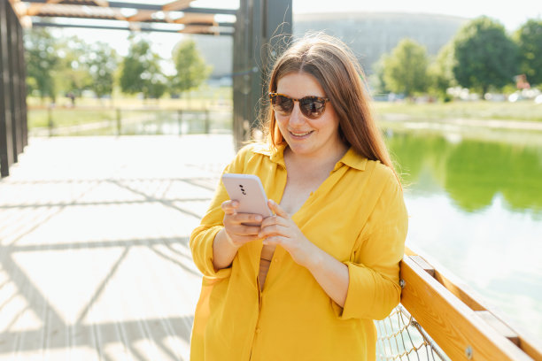 美丽时髦的女人在夏日的公园里散步，拿着手机。电话沟通。城市生活方式的概念。旅行者图片下载