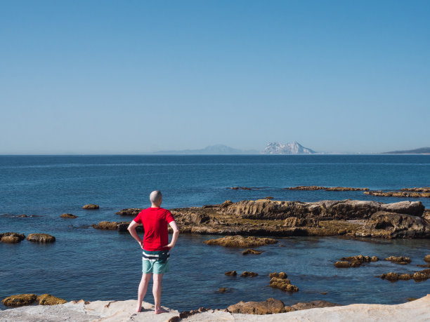 一个面目模糊的白头男子凝视着窗外的景色。在背景中你可以看到直布罗陀的岩石和摩洛哥阿特拉斯(非洲大陆的山脉)图片下载