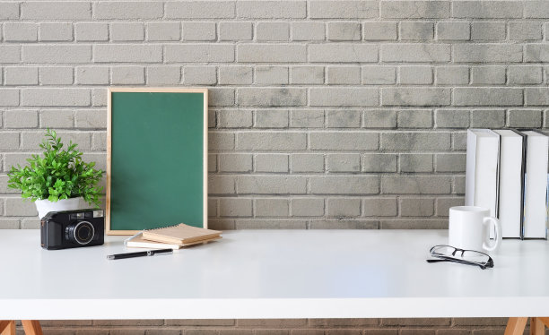 创意工作场所，绿色黑板，相机，咖啡杯和书在白色的桌子上。复制信息内容的空间。图片下载