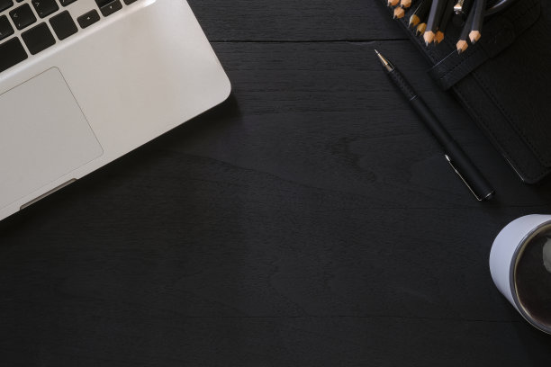 黑色木制背景的笔记本电脑、咖啡杯和铅笔。前视图。图片下载