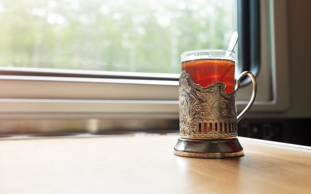 火车车厢的窗户前的桌子上放着一杯装在杯架里的茶。图片下载