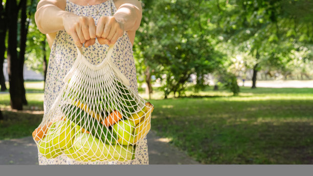 编织网袋蔬菜和水果在一个女人的手中。图片下载