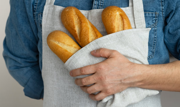 手里拿着用亚麻布毛巾裹着的刚出炉的面包。法国面包。面包店。食物图片下载