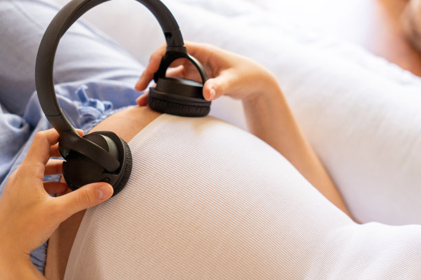 怀孕的女人听音乐。听音乐的孕妇。妈妈肚子听耳机的声音。怀孕的概念，母性，对婴儿的期望。图片下载