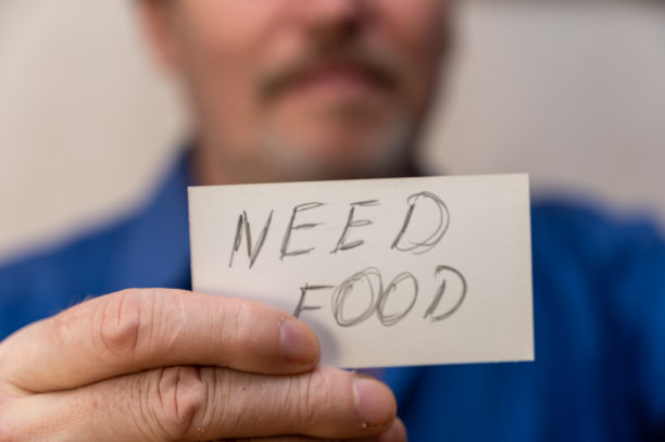 需要食物。纸上的字是锯齿状的灰色字母。一名男子拿着写有手写文字的长方形白纸站在面前。一个成熟男人的手特写。图片下载