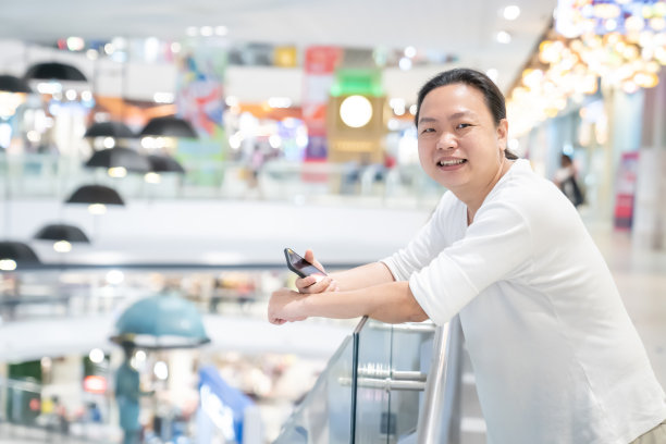 身穿白色t恤的亚洲、泰国长发男子在百货店内玩手机(白色屏幕)。图片下载