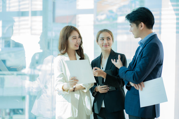 在一间高调的办公室里，一个年轻的多民族商务团队坐在笔记本电脑上，微笑着做着文书工作。亚洲商务人士团队汇聚于现代办公设计与概念规划领域图片下载