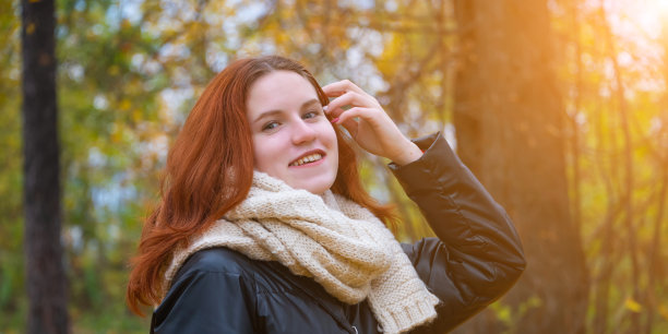 在秋天的自然和明亮的阳光的背景下，穿着夹克和围巾的红头发微笑的女孩的肖像图片下载