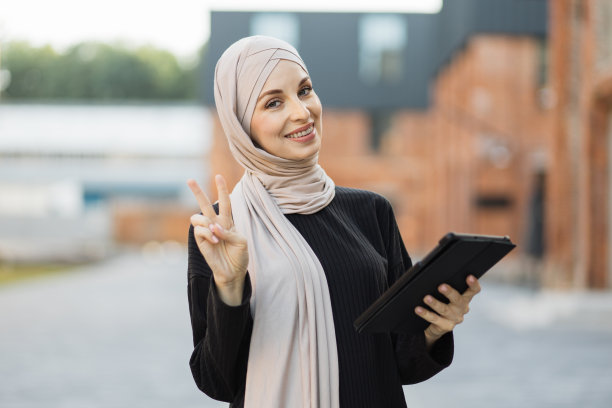 快乐的阿拉伯女孩站在户外和检查电子邮件的数码小玩意。图片下载