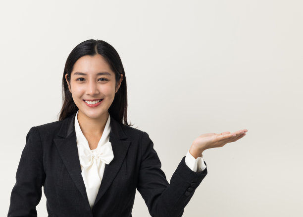 年轻的亚洲商业女性微笑手掌向上的空白空间持有的东西在孤立的白色背景。25岁左右的女性在摄影棚拍摄西装人像。图片下载