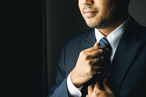 自信的商人在酒店房间的窗边用领带调整经典的蓝色西装。一个帅哥在婚礼上穿了一套漂亮的西装。图片下载