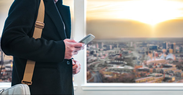 穿着黑色外套的商人用手机看日落的天空。图片下载