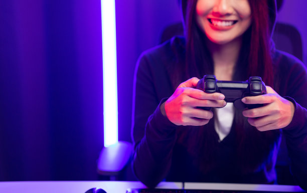 玩视频游戏。年轻的亚洲漂亮女人坐在椅子上握着操纵杆在客厅。快乐女性专业Streamer华人穿着连帽衫在黑暗的房间霓虹灯在线游戏。图片下载