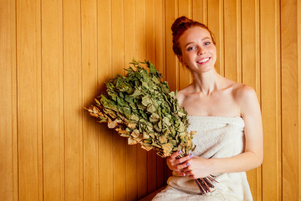 红发姜女在澡堂里蒸着俄罗斯束桦木扫帚。她享受芬兰温泉蒸桑拿，减肥的概念。脸上毛孔开放图片下载