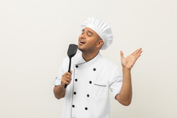 超级明星唱歌厨艺大师。年轻快乐的亚洲厨师穿着制服，在孤立的白色背景下享受着歌声和舞蹈。印度男人占领餐馆和酒店。图片下载
