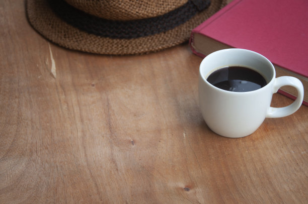 咖啡杯与书和棕色帽子在木制书桌。副本的空间。图片下载