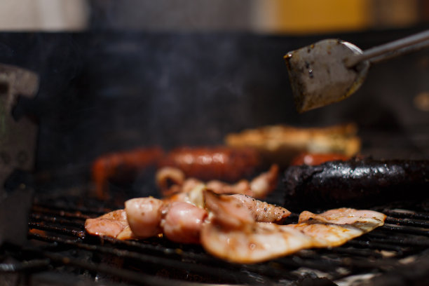 用金属钳在黑色的烧烤架上转动沸腾的土豆和香肠。图片下载