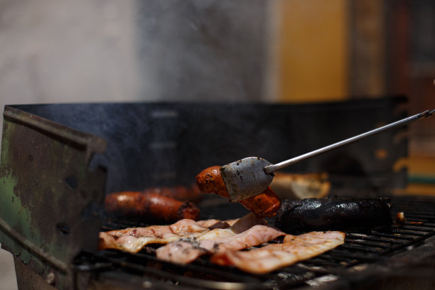 用金属钳在黑色的烧烤架上转动沸腾的土豆和香肠。图片下载