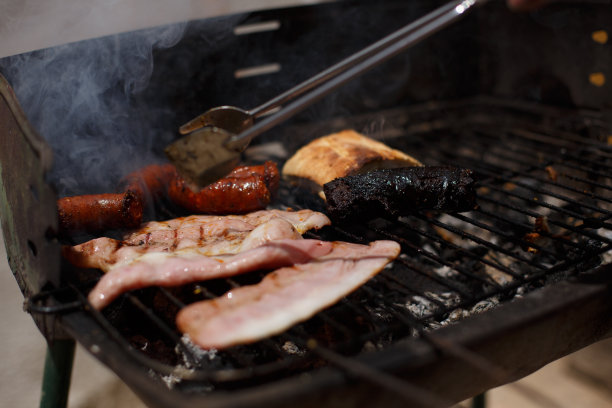 用金属钳在黑色的烧烤架上转动沸腾的土豆和香肠。图片下载