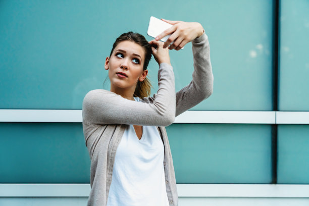快乐有吸引力的潮女孩拍照片的手机和微笑在城市街道。图片下载
