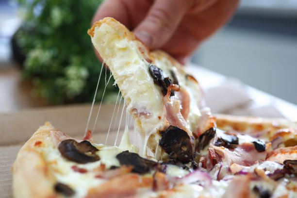 男性手臂在工作桌上拿着一大块新鲜的硬皮披萨图片下载