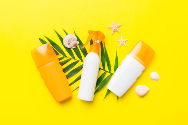 防晒喷雾瓶。瓶与防晒霜和海贝壳与热带绿色树叶的颜色背景，俯视图图片下载