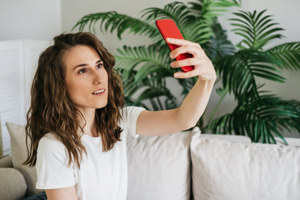 这个女孩手里拿着一个手机。一个女人在互联网上写信息，看图片，搜索信息。女孩为社交网络自拍。女人微笑着坐在家里的沙发上放松图片下载