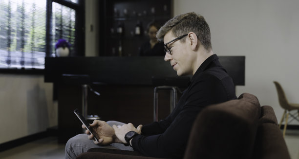 快乐英俊的商人自信地戴着眼镜，在酒店大堂用智能手机查看邮件和信息。图片下载