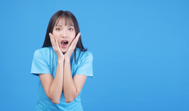 激动的亚洲妇女手在嘴震惊惊讶销售产品的拷贝空间在蓝色的背景。开朗的小女孩情绪激动，惊讶地尖叫着哇哇什么就孤立了。购物的概念图片下载