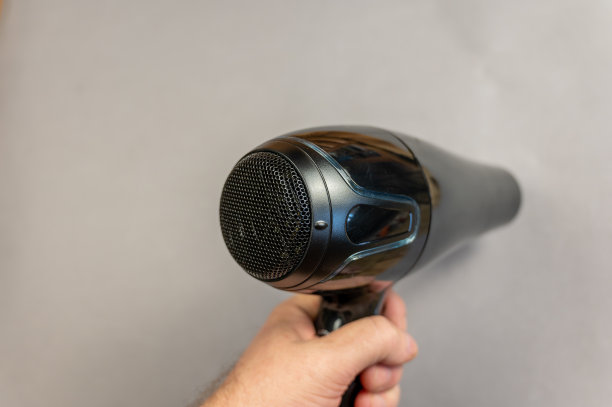 一个男人手里拿着一个电吹风。一种黑色的电装置，发出有向的热空气流。灰色的背景。在房间里面。特写镜头。有选择性的重点。图片下载