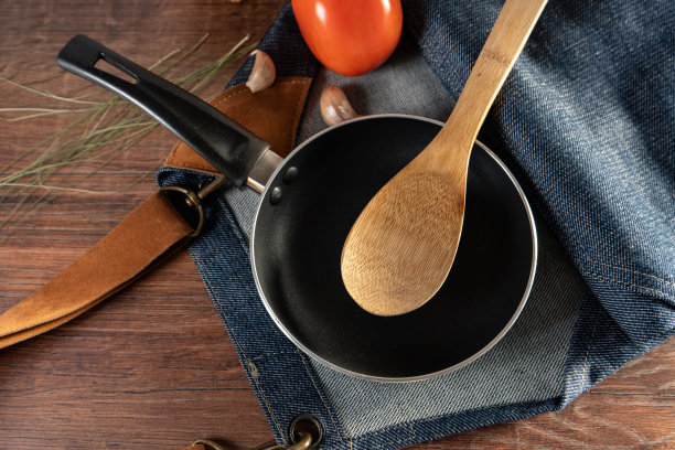 一个平底锅，一个勺子，一条围裙放在一张木桌上。图片下载