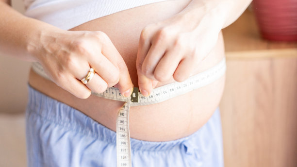 孕妇测肚子。幸福美丽的孕妇用卷尺量肚子。孕、药保健理念。图片下载